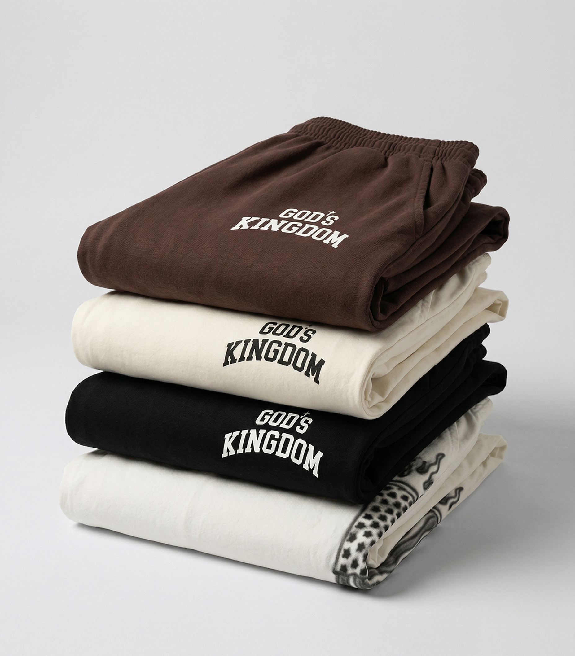 Stack of folded shirts with 'God's Kingdom' text on a light gray background